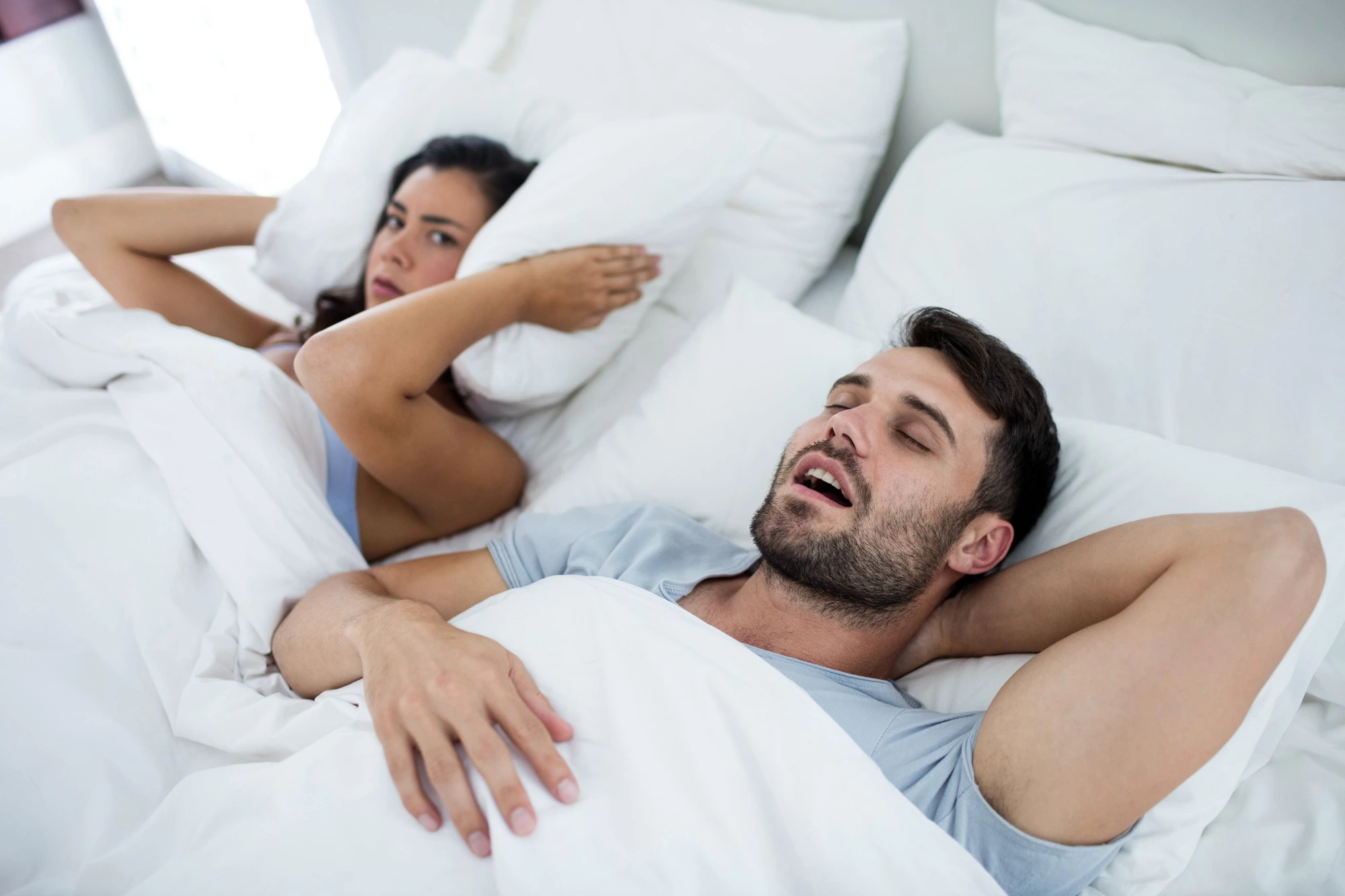 Homem roncando e mulher tapando os ouvidos com travesseiro